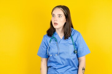 Young caucasian doctor woman wearing blue medical uniform stares aside with wondered expression has...