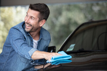 happy man polishing his car with microfiber cleaning cloth