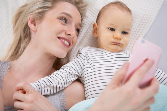 woman with a baby doing a selfie lying on blanket