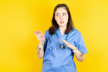 Displeased Young caucasian doctor woman wearing blue medical uniform keeps hands towards empty...
