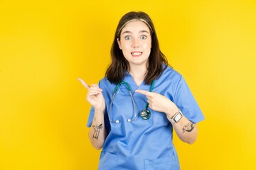 Young caucasian doctor woman wearing blue medical uniform points at copy space indicates for...