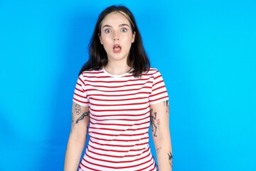 Shocked beautiful young woman wearing striped T-shirt stares bugged eyes keeps mouth opened has surprised expression. Omg concept