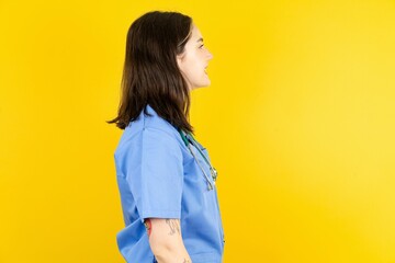 Profile portrait of nice Young caucasian doctor woman wearing blue medical uniform look empty space toothy smile