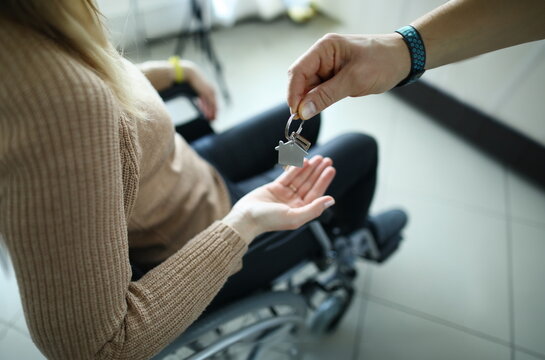 Woman is sitting in wheelchair and keys are handed over to her. Getting housing for disabled people concept