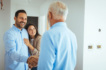 Obraz premium Real Estate Agent showing a house under construction to a couple and greeting them with a handshake. Friendly Real Estate Agent and young couple shaking hands standing in hallway