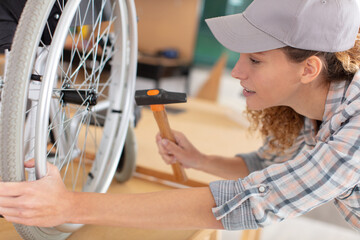 woman is repairing a wheelchair using a hammer