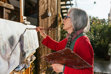 Senior woman painting on canvas in garden