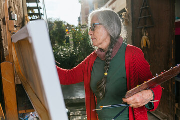 Senior woman painting on canvas in garden