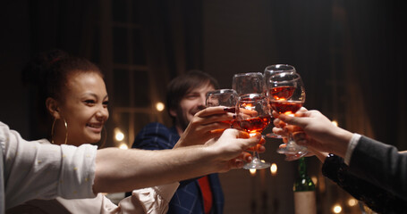 Happy friends celebrating christmas or graduation together, having a dinner party, clinking their glasses with wine, talking and smiling - celebration, real people