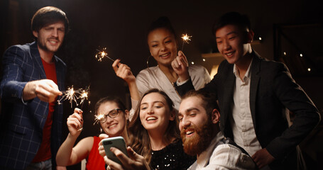 Positive multiethnic student friends celebrating together, having video chat with their friends or parents, cheering about christmas or graduation and smiling - communication, real people 