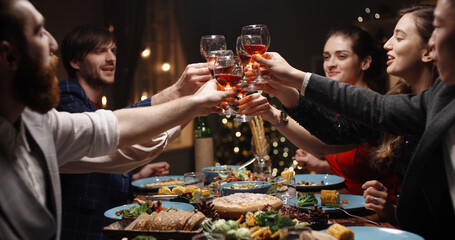 Positive multiethnic student friends celebrating together, toasting to something at dinner party table and clinking their glasses - celebration, real people, emotion 