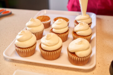 Crop person decorating cupcakes with whipped cream