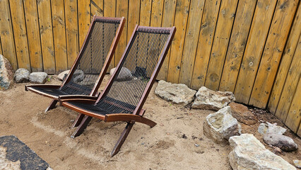 Two old wooden chairs on the sand against a wooden wall, photo