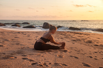 Fototapeta na wymiar Young pretty lady meditating workout on sea beach, doing yoga pose. Cute woman perform sport exercises to restore strength and spirit at ocean sunrise. Healthy lifestyle concept. Copy ad text space