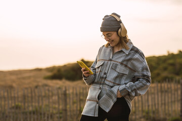 Happy young lady using smartphone and listening to music in headphones in countryside