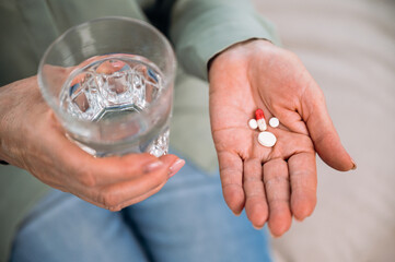 Woman holding pills and glass of water in hands