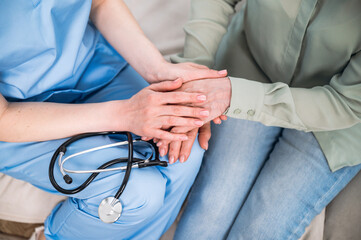 Fototapeta premium Woman doctor holding patient hands, caring elderly female at medical appointment