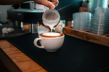 Barista hand pouring milk into coffee making a cappuccino. Professional barista preparing coffee on the counter.