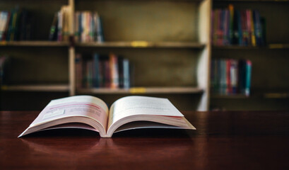 On a wooden table, there's an open book with a library visible in the background. A stack of books nearby adds to the theme of educational learning.