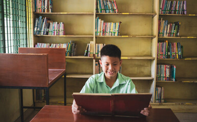 At the library, a young boy of Asian descent is deeply engrossed in reading a book during his break.