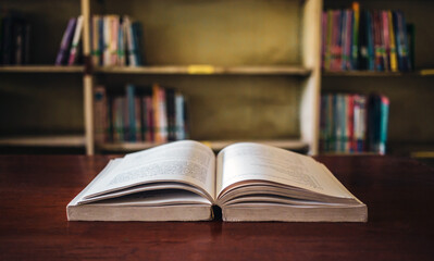 On a wooden table, there's an open book with a library visible in the background. A stack of books nearby adds to the theme of educational learning.