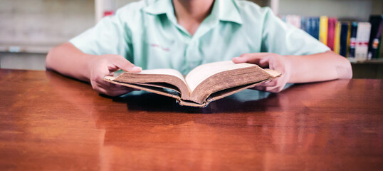 In this picture, we can see a boy's hand as he opens a book in a library. The shelves in the background are filled with numerous books.