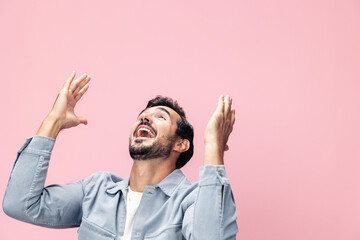 Fashion portrait of a brunette man with a beard happiness victory raised his hands with his fist up on a pink background in a white T-shirt smile and joyful emotion on his face, copy space - Powered by Adobe
