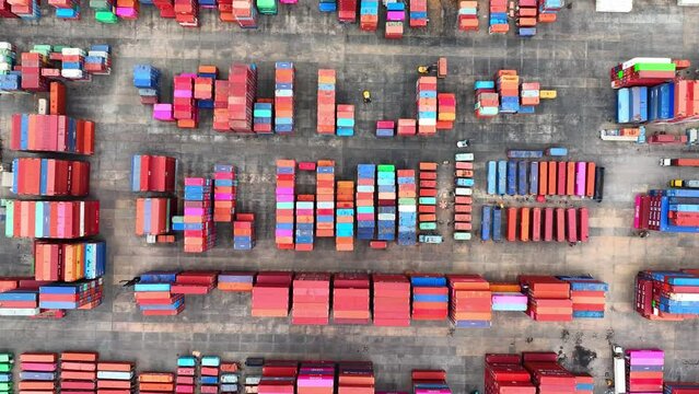 A sprawling container yard, bustling with activity, seen from above through the lens of a drone, showcasing organized stacks of cargo containers.
