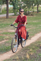 Cheerful young female cyclist riding bike near trees in park