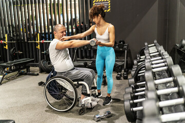 Fototapeta na wymiar In a display of strength and inclusivity, a person in a wheelchair engages in a workout session with the help of a supportive female fitness instructor. 