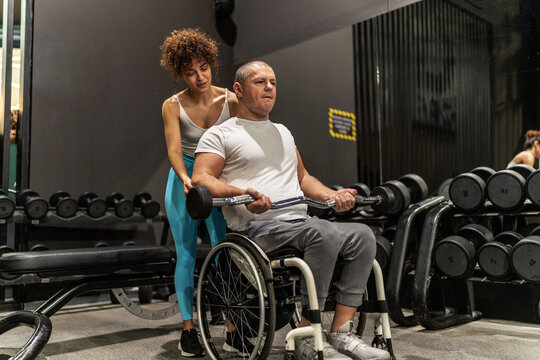 In a display of strength and inclusivity, a person in a wheelchair engages in a workout session with the help of a supportive female fitness instructor.	
