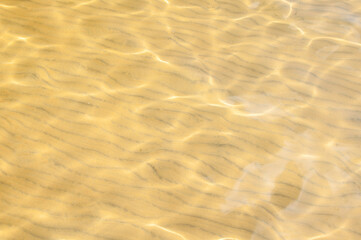 Patterned sandy lake bottom with sunlight reflecting on water surface above it as a background, horizontal shot