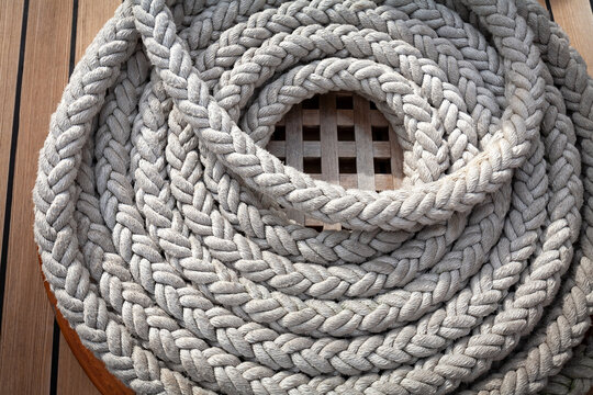 On the wooden deck of the mast yacht, a white anchor rope is folded into a round bug.