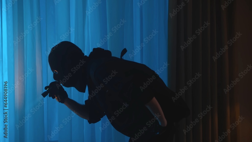 Wall mural shot of a burglar, intruder standing in the house, leaning forward with a flashlight on. the man is 