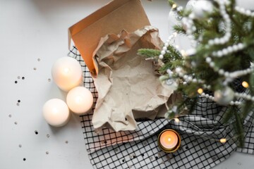 Open carton gift box with craft paper under Christmas tree with candles and confetti