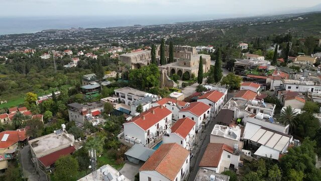 Drone flight over residential neighborhood towards the ruins of Bellapais Abbey monastery, religion and historic architecture in North Cyprus