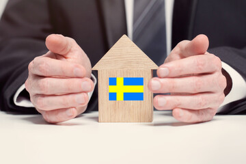 Businessman hand holding wooden home model with Swedish flag. insurance and property concepts