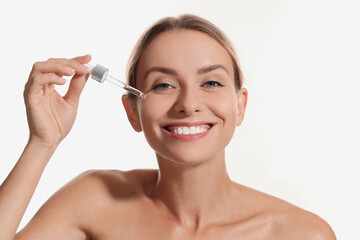 Obraz na płótnie Canvas Beautiful woman applying cosmetic serum onto her face on white background