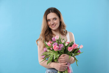 Happy young woman with bouquet of beautiful tulips on light blue background