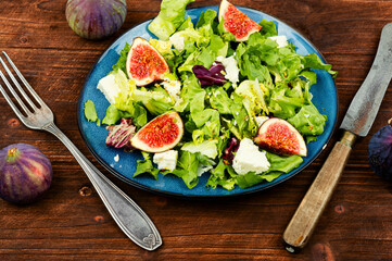 Salad with figs, herbs and cheese on wooden table.