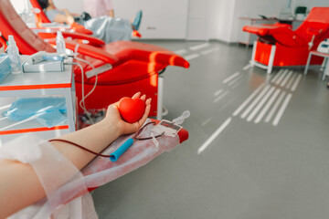 Young woman making blood donation in hospital. A woman donates blood while holding a red heart. Blood donation.