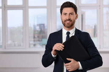 Happy real estate agent with leather portfolio indoors. Space for text