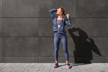 Beautiful woman in stylish gym clothes near dark grey wall on street, space for text