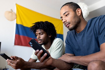 Two latino boys looking at the mobile phone with the Colombian flag behind them.