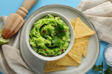 Delicious guacamole served with nachos chips on light blue table, flat lay