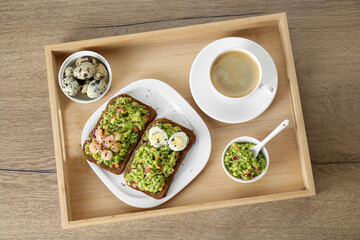 Slices of bread with tasty guacamole, eggs, shrimp and coffee on wooden table, top view