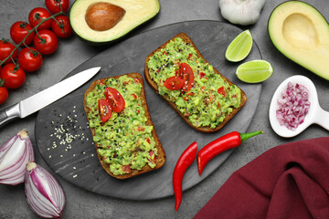 Slices of bread with tasty guacamole and ingredients on grey table, flat lay