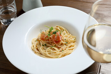 Tasty spaghetti with prosciutto and microgreens served on wooden table, closeup. Exquisite presentation of pasta dish