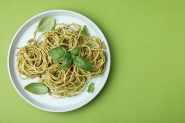 Delicious pasta with pesto sauce and basil on light green background, top view. Space for text