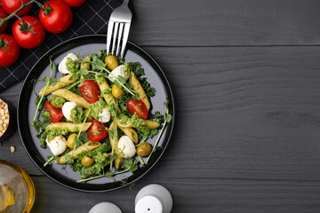 Delicious pesto pasta salad, ingredients and fork on gray wooden table, flat lay. Space for text